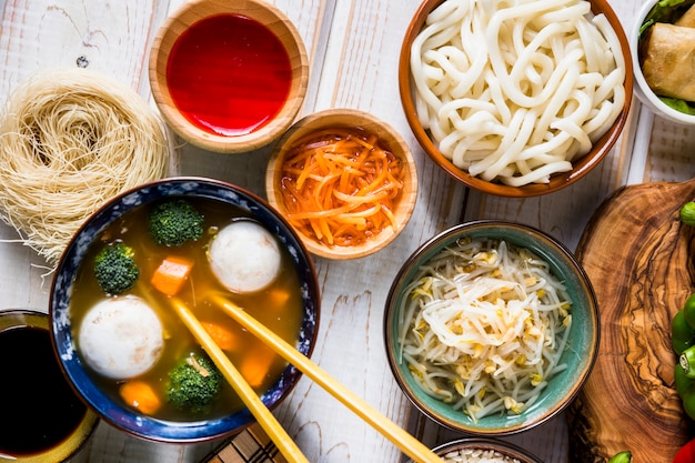 Uma visão aérea de peixe tailandês e sopa tigela de legumes com macarrão udon; molho e feijão brota na mesa branca