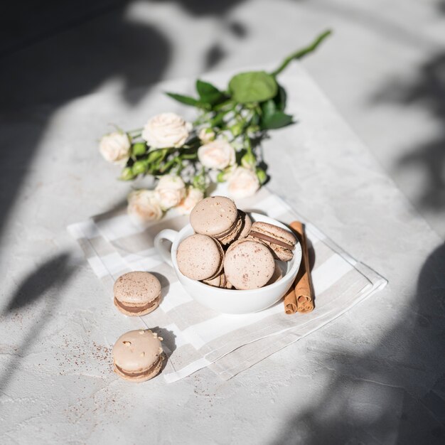 Uma visão aérea do buquê de rosa com macaroons de canela em copo branco no pano de fundo cinza concreto texturizado