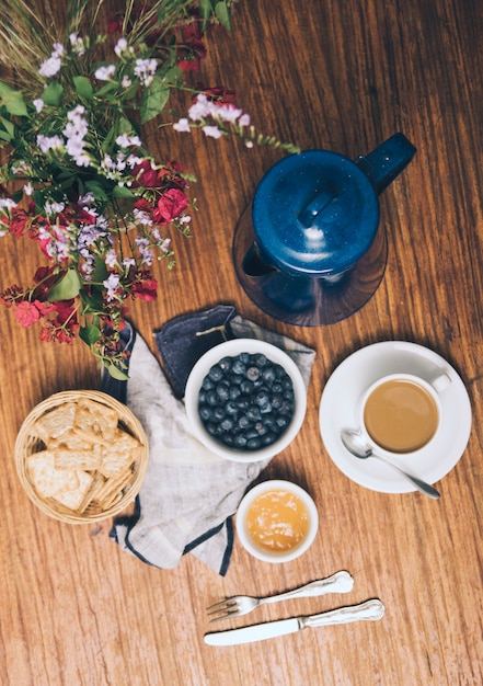 Uma visão aérea do vaso; amoras; biscoitos; geléia; xícara de café e bule em pano de fundo de madeira