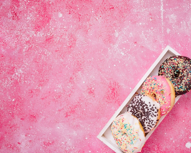 Foto grátis uma visão elevada de donuts na caixa de madeira branca na esquina do fundo rosa