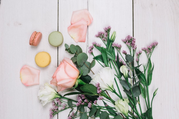 Uma visão elevada de macaroons e buquê de flores frescas em pano de fundo de madeira