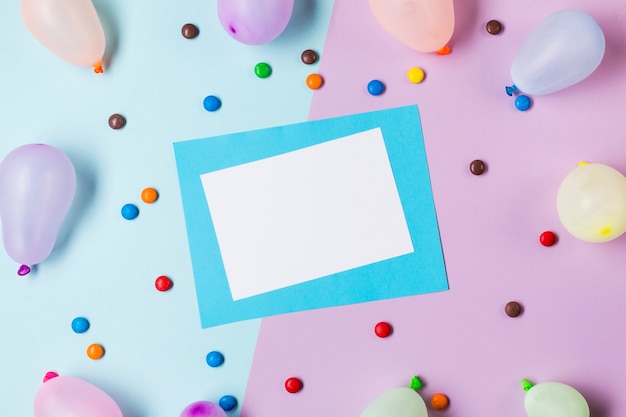 Uma visão elevada de papel branco e azul, rodeado de pedras preciosas e balões em pano de fundo azul e rosa