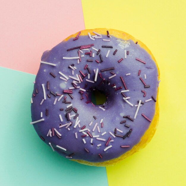 Uma visão elevada do donut roxo com granulado em fundo colorido