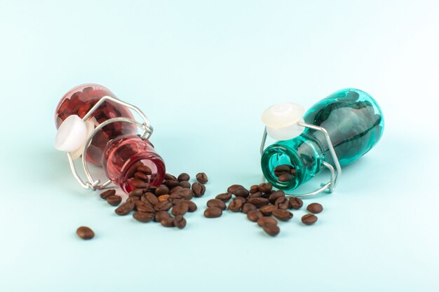 Uma visão frontal das sementes de café marrom dentro de potes de vidro coloridos na superfície azul