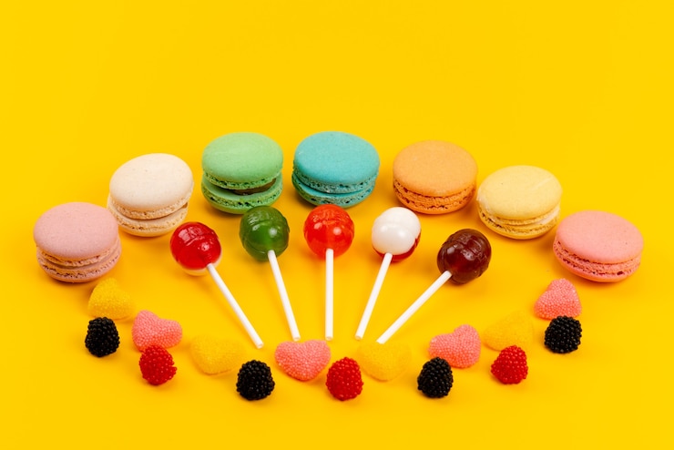 Foto grátis uma visão frontal de macarons e pirulitos junto com geleias isoladas em amarelo, bolo de açúcar doce doce