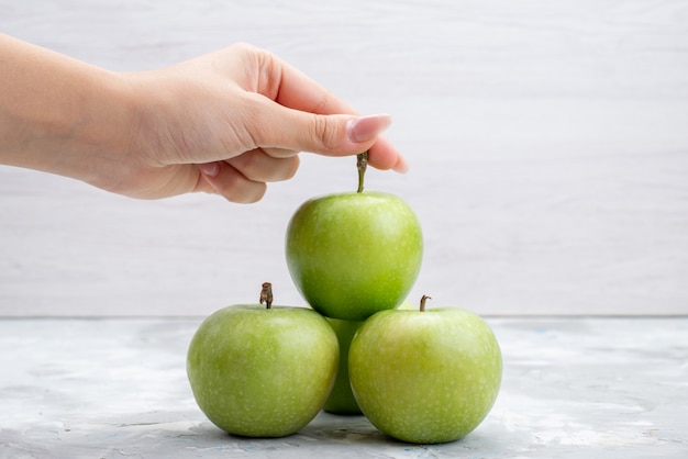 Uma visão frontal de maçãs verdes frescas suaves e suculentas na árvore de mesa clara com frutas frescas