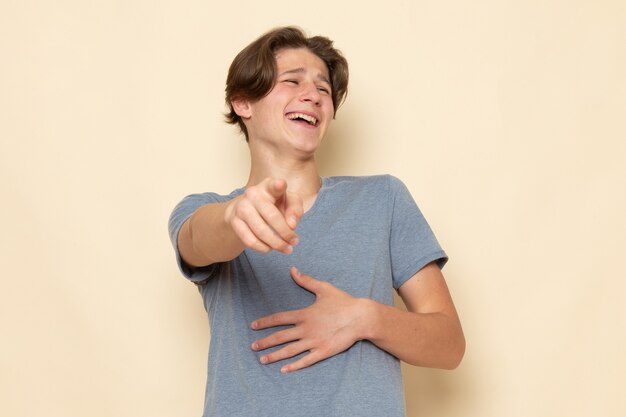 Uma visão frontal de um jovem do sexo masculino com camiseta cinza posando de rir