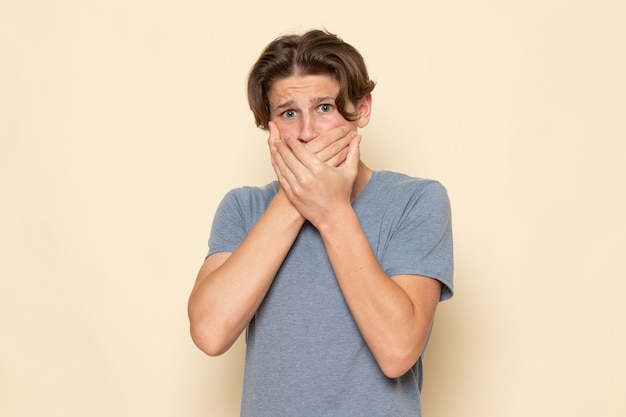 Uma visão frontal de um jovem do sexo masculino com uma camiseta cinza posando segurando a boca