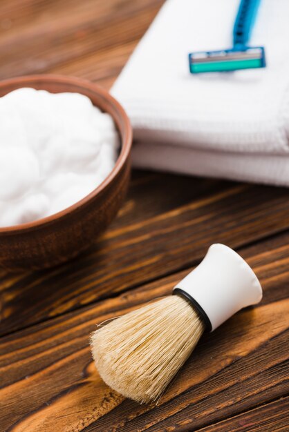 Uma visão geral da escova sintética de barbear com espuma desfocada; guardanapo e navalha na mesa de madeira