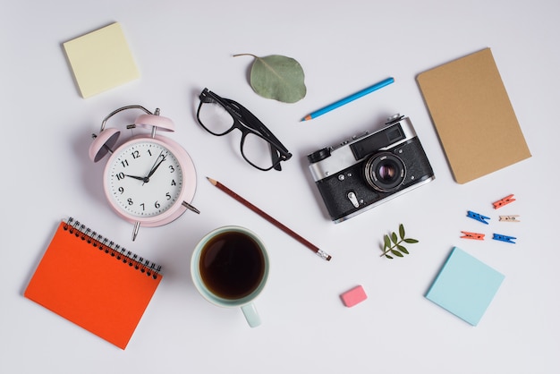 Uma visão geral do despertador; Óculos; Câmera; xícara de café e material de escritório em fundo branco