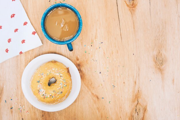 Uma visão geral do donut; xícara de café e lenço de papel na mesa de madeira