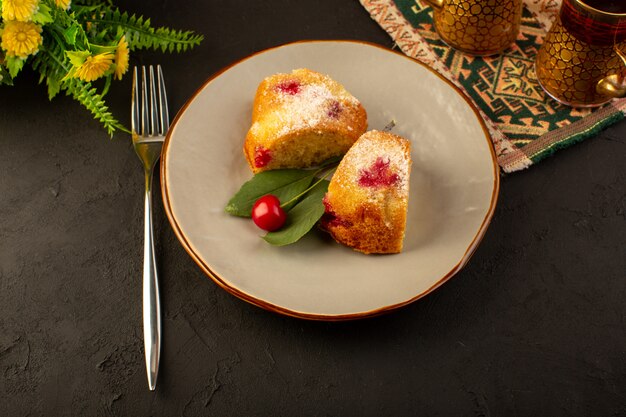 Uma vista de cima assou fatias deliciosas de bolo de frutas com cerejas vermelhas e açúcar em pó dentro de um prato redondo cinza escuro