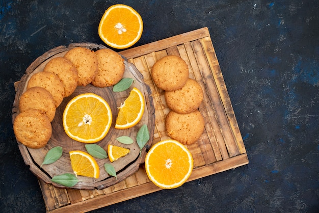 Uma vista de cima biscoitos com sabor de laranja com fatias de laranja frescas no fundo escuro.