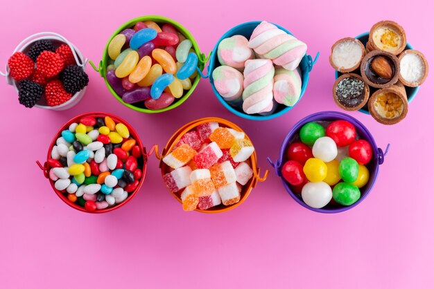 Uma vista de cima bombons e marmeladas coloridas e deliciosas dentro de cestas na cor rosa