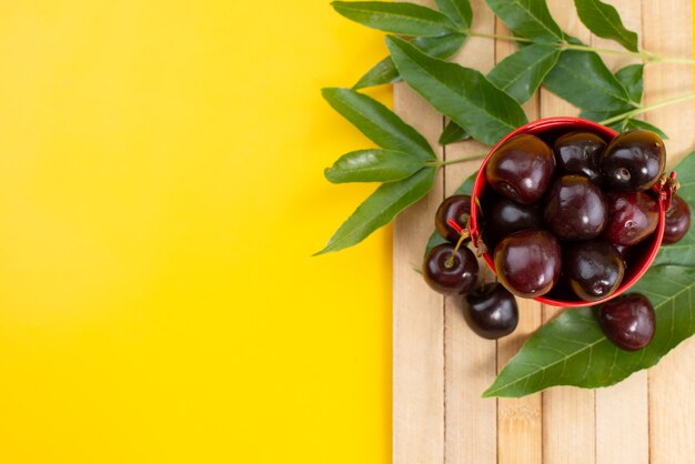 Uma vista de cima cerejas vermelhas maduras e suculentas dentro de uma cesta em uma mesa de madeira marrom e frutas amarelas no verão