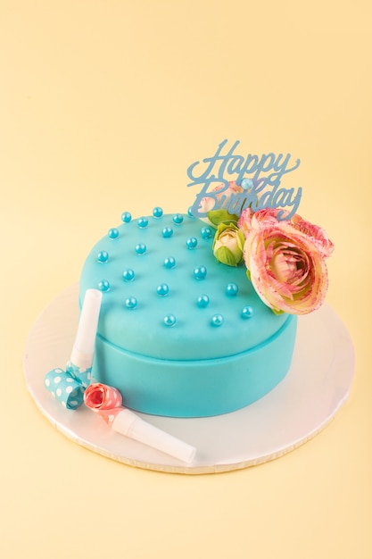 Uma vista de cima do bolo de aniversário azul com uma flor no topo da mesa amarela.