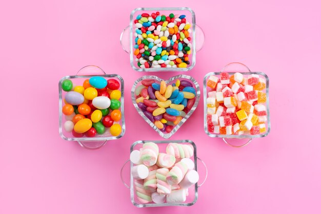 Uma vista de cima doces e marshmallows coloridos dentro de copos em uma mesa rosa, cor doce açúcar