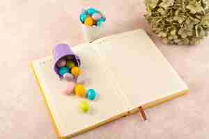 Foto grátis uma vista de cima dos doces coloridos com o caderno na mesa rosa