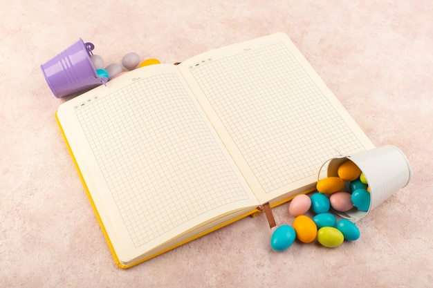 Uma vista de cima dos doces coloridos com um caderno na mesa rosa, cor de doce doce