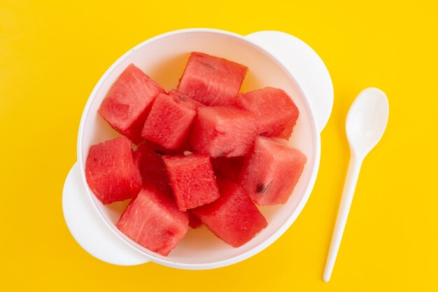 Uma vista de cima em fatias de melancia fresca dentro de um prato de plástico branco sobre uma mesa amarela, cor de frutas do verão