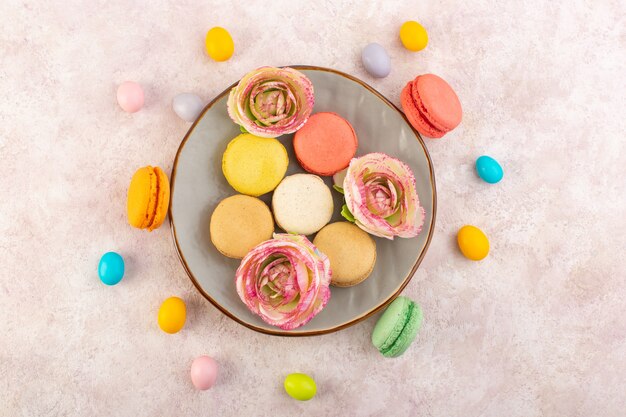 Uma vista de cima macarons franceses coloridos com rosas na mesa rosa bolo biscoito açúcar doce