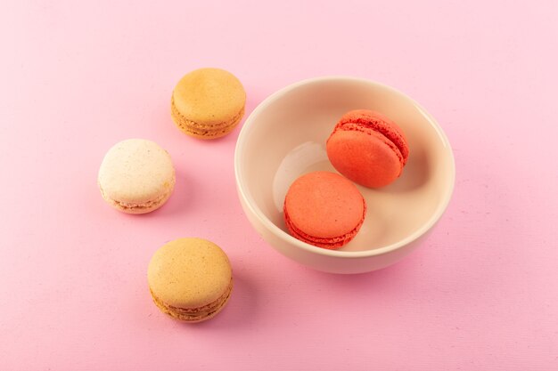 Uma vista de cima macarons franceses coloridos dentro e fora do prato na mesa rosa