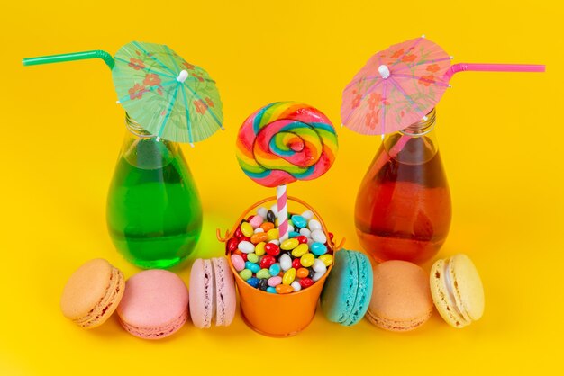 Uma vista de cima, macarons franceses coloridos junto com doces e bebidas diferentes em amarelo, biscoito de bolo doce