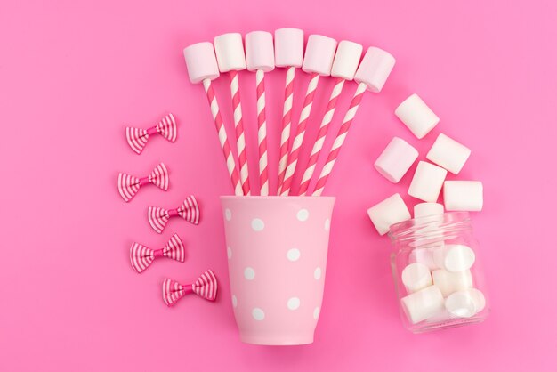 Uma vista de cima marshmallows brancos com varas e laços rosa na mesa rosa, cor de açúcar doce