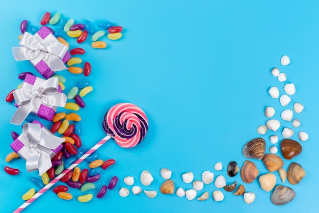 Uma vista de cima, pirulitos e geleias coloridas doces junto com conchas do mar no azul, confeitaria doce de açúcar