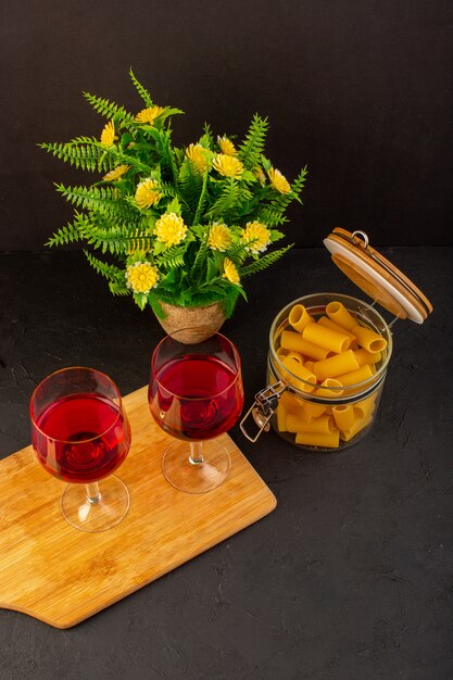 Uma vista de cima, taças de vinho na mesa de madeira marrom, junto com flores e massa italiana crua na mesa escura, bebem bebida alcoólica