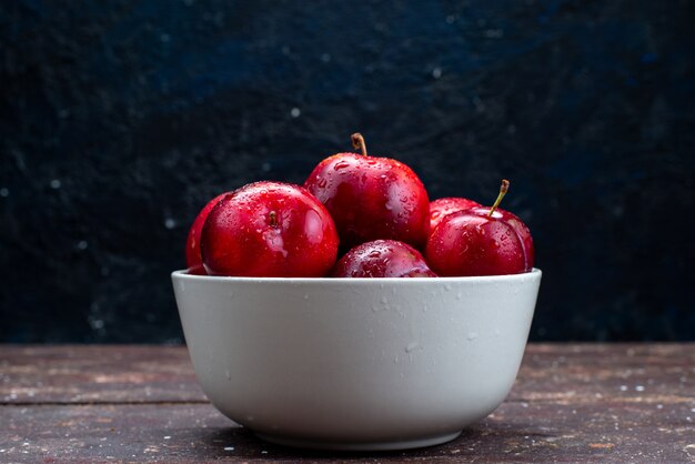 Uma vista frontal ameixas vermelhas frescas maduras e maduras dentro de um prato branco na mesa de madeira suco de polpa de frutas