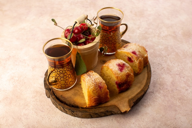 Uma vista frontal assada de bolo de frutas delicioso fatiado com cerejas vermelhas dentro e açúcar em pó em uma mesa de madeira com chá de cerejas frescas em rosa