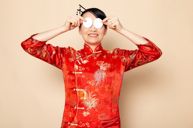 Uma vista frontal bela gueixa japonesa no tradicional vestido japonês vermelho com varas de cabelo posando segurando pouco algodão branco elegante sorrindo sobre a cerimônia de creme de fundo japão