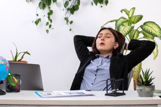 Uma vista frontal bela jovem empresária de jaqueta preta e camisa azul espirros desejando dormir na frente do escritório de trabalho de negócios de mesa