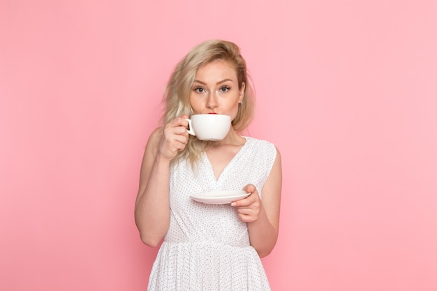 Uma vista frontal bela moça de vestido branco, bebendo um chá