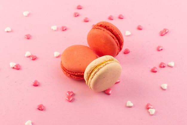 Uma vista frontal colorida de macarons franceses redondos formados e deliciosos na mesa rosa