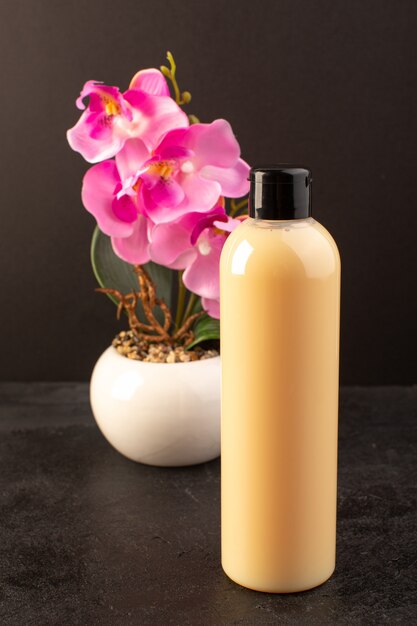 Uma vista frontal creme shampoo de garrafa de plástico colorido pode com tampa preta com flor isolada no fundo escuro cosméticos beleza cabelo