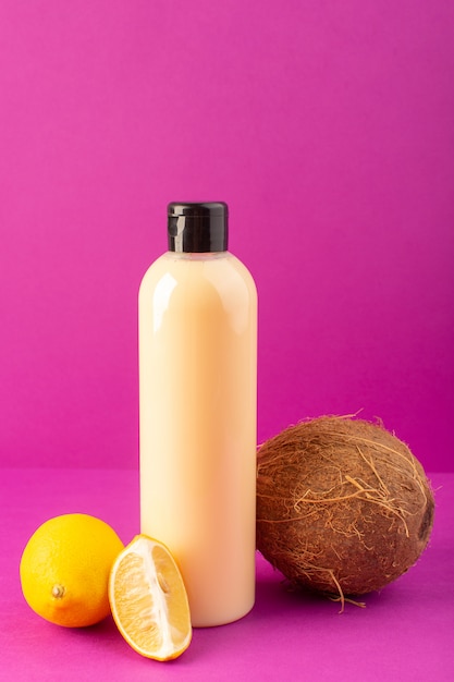 Uma vista frontal creme shampoo de plástico de garrafa colorida pode com tampa preta junto com limões e coco isolado no fundo roxo cosméticos beleza cabelo