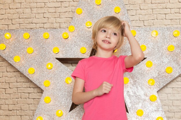 Uma vista frontal criança bonitinha em jeans rosa camiseta cinza na estrela projetado carrinho amarelo e luz de fundo