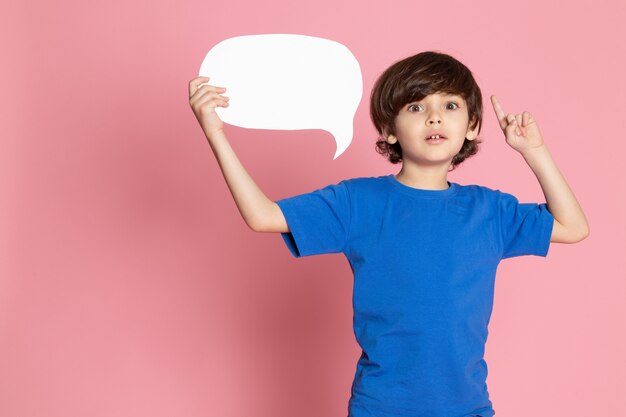 Uma vista frontal criança menino adorável doce em t-shirt azul segurando placa branca no espaço rosa