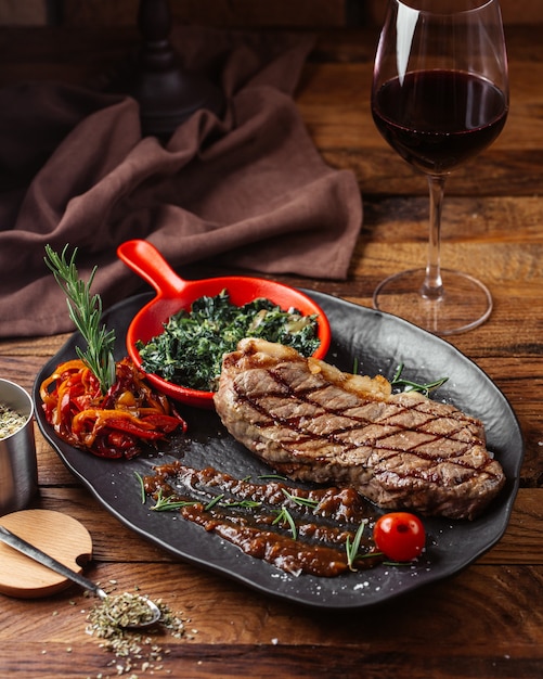 Uma vista frontal de carne frita com verduras dentro de um prato escuro na mesa de madeira marrom.