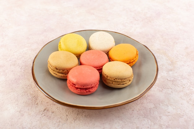 Uma vista frontal de macarons franceses coloridos dentro do prato na mesa rosa