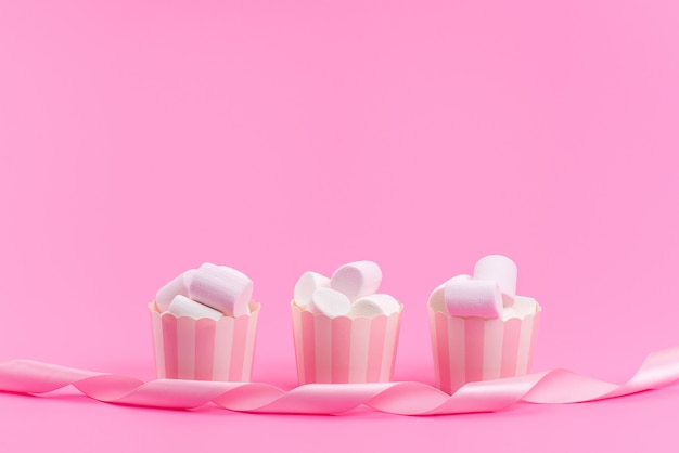 Uma vista frontal de marshmallows brancos dentro de pacotes de papel rosa isolados em rosa