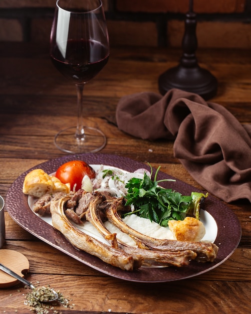 Uma vista frontal de ossos de carne frita com verduras e tomate na mesa de madeira marrom refeição comida carne