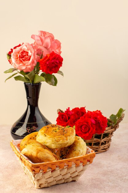 Uma vista frontal de rosas vermelhas lindas e flores dentro do jarro preto junto com qogals dentro da caixa de pão isolada na mesa e rosa
