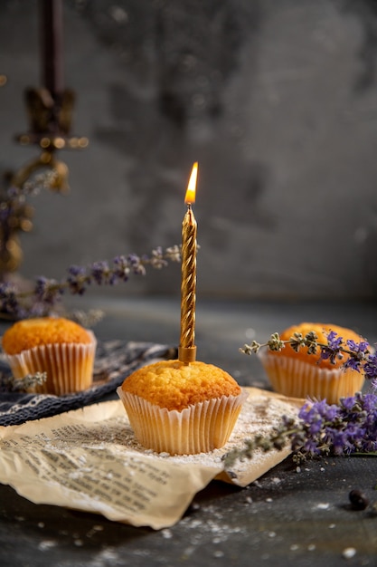 Uma vista frontal deliciosos bolinhos com velas e flores roxas na mesa cinza biscoito chá biscoito doce