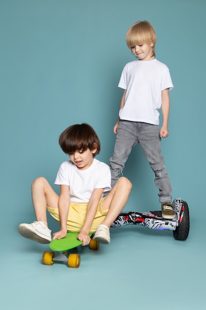 Uma vista frontal dois meninos adorável doce bonito feliz andar de scooter e segway no chão azul