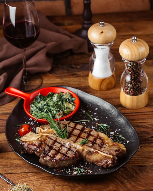 Uma vista frontal fatias de carne frita com verduras dentro de um prato preto com um copo de vinho na mesa de madeira marrom