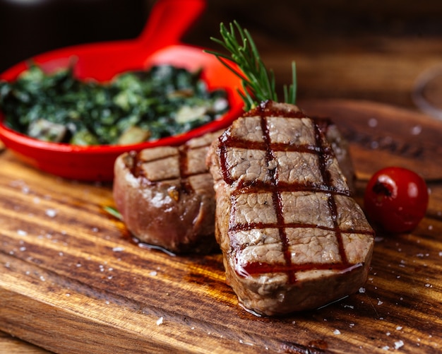 Uma vista frontal fechada de carne frita com molho e verduras junto com um copo de vinho na mesa marrom