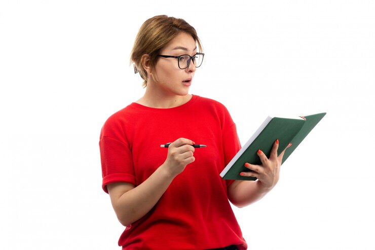 Foto grátis uma vista frontal jovem aluna em t-shirt vermelha segurando o caderno escrevendo notas surpreso no branco